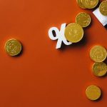 Moedas de ouro sobre um gráfico de mercado com símbolo de porcentagem, em fundo laranja