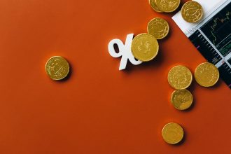 Moedas de ouro sobre um gráfico de mercado com símbolo de porcentagem, em fundo laranja