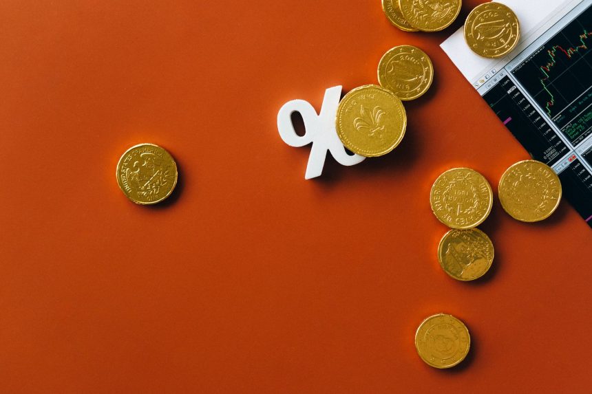 Moedas de ouro sobre um gráfico de mercado com símbolo de porcentagem, em fundo laranja