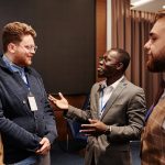 Grupo diverso de pessoas reunido em ambiente interno, participando de uma discussão coletiva em torno de uma mesa