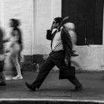Homem caminhando na rua com uma pasta, cercado por pedestres em movimento.
