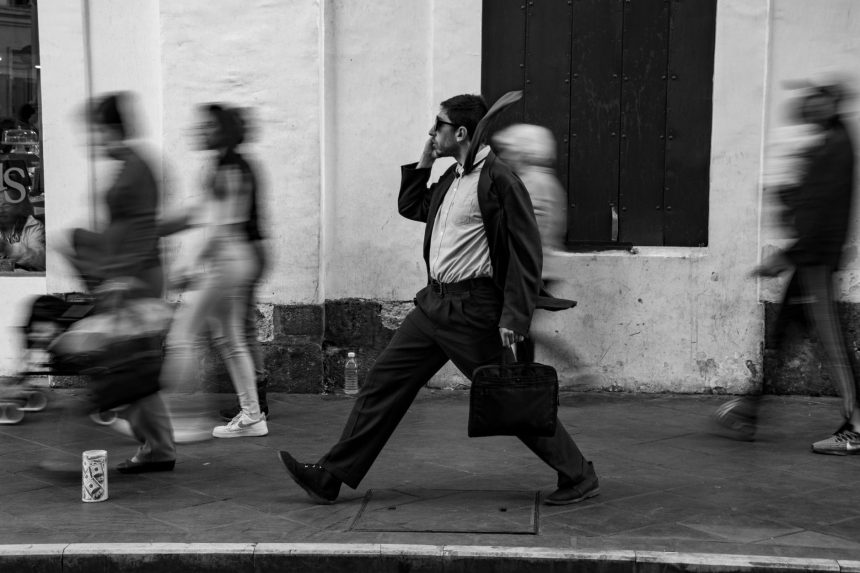 Homem caminhando na rua com uma pasta, cercado por pedestres em movimento.