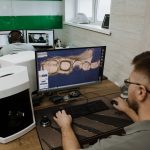 Profissional visto de costas trabalhando em um laboratório odontológico moderno na criação de um modelo 3D de dentes em um computador.