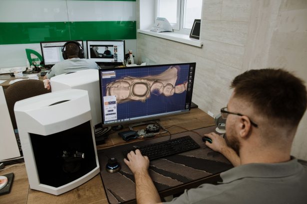Profissional visto de costas trabalhando em um laboratório odontológico moderno na criação de um modelo 3D de dentes em um computador.